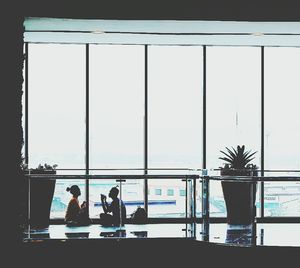 People working on table by sea against sky seen through window