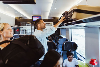 Mid adult man arranging suitcase on shelf in train during family trip