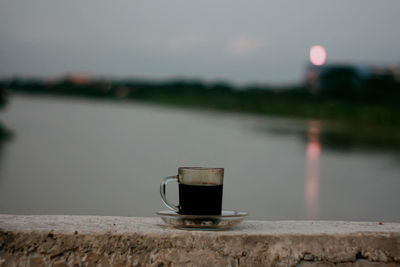 Close-up of coffee cup against lake