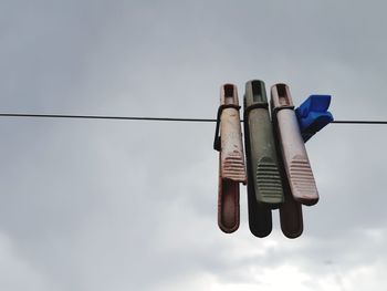 Low angle view of clothespins hanging on rope against sky
