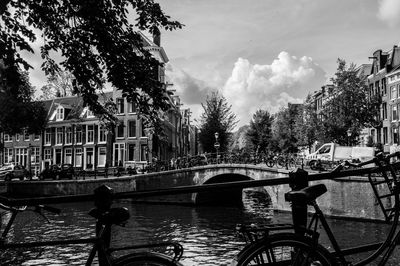 Bicycle by canal against sky in city