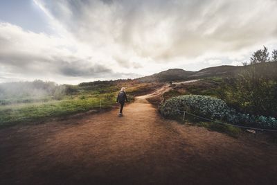 Rear view of man walking on landscape against sky