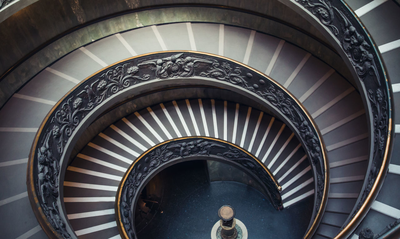 steps, indoors, steps and staircases, staircase, railing, lifestyles, men, high angle view, leisure activity, architecture, built structure, spiral staircase, spiral, person, standing, pattern, arch, low angle view