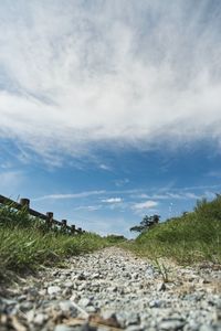 Surface level of dirt road on field against sky
