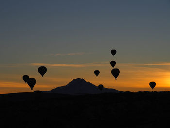 Silhouette hot air balloons on landscape against sky during sunset