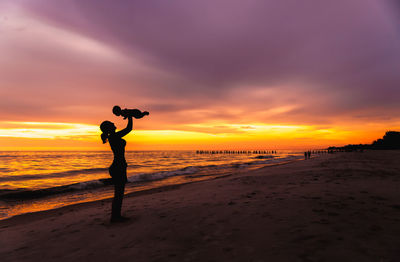 Rear view of woman standing at beach against sky during sunset