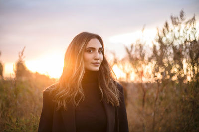 Portrait of young woman standing against trees during sunset