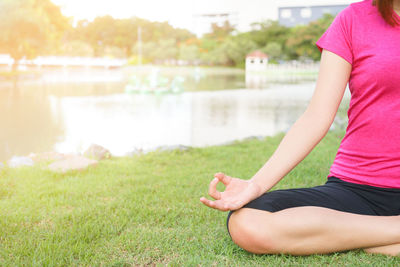 Midsection of woman sitting on grass by lake