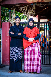 Portrait of smiling couple standing by gate outdoors