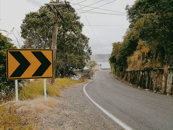 Road sign by trees against sky