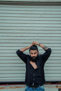 Bearded man tying hair while standing against shutter