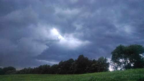 Low angle view of trees on field against storm clouds