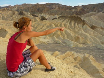 Woman pointing while sitting on rock in desert