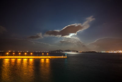 Night view of athens piraeus harbor with moon partially hidden by clouds, greece