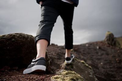 Low section of man climbing on rocky mountains against cloudy sky