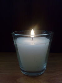 Close-up of illuminated candle on table against black background