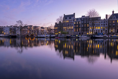 River by illuminated buildings against sky at dusk