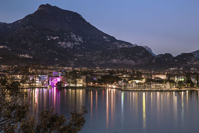 Scenic view of lake by illuminated city against sky at night, garda lake