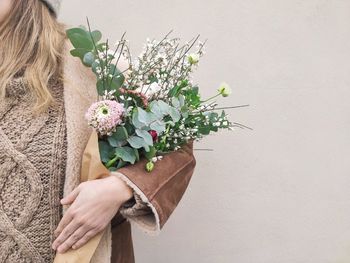 Midsection of woman holding flowering plant against white wall