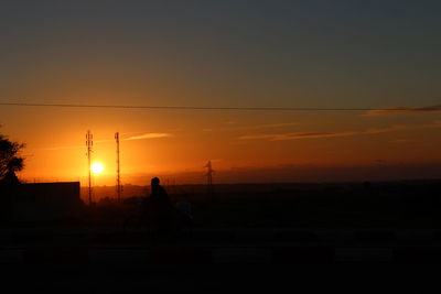 Silhouette people sitting on landscape against orange sky