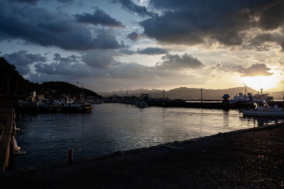 Boats moored in harbor at sunset