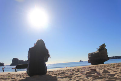 Man sitting on beach by sea against clear sky