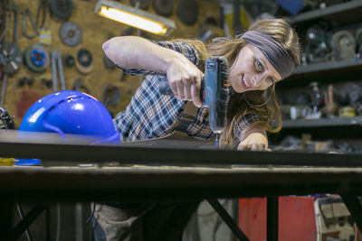Low angle view of woman drilling on table in workshop
