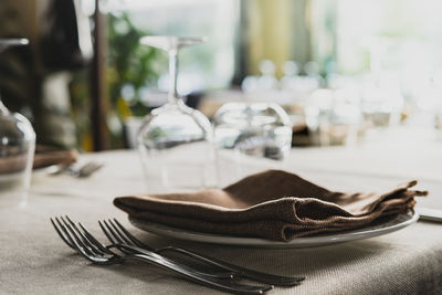 Close-up of plate with napkin and forks on table in restaurant