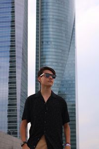 Young man wearing sunglasses standing against building in city