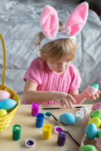 Little girl in easter bunny ears painting colored eggs. easter at home and craft concept.