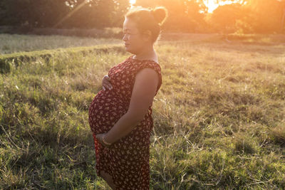 Pregnant woman standing in the meadow warm tones.