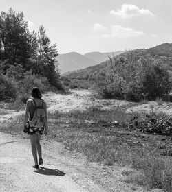 Rear view of woman walking on field against sky