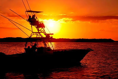 Silhouette sailboat in sea against orange sky