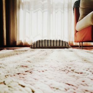 Pillow by rug against window curtain at home