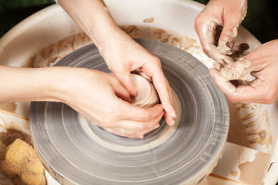 Close-up of a woman potter teaches a student sculpts from a brown clay on a potter's wheel 