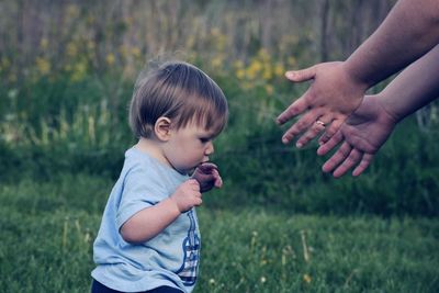 Cropped hands of mother by baby boy on grassy field