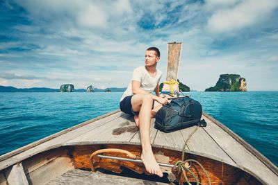 Man traveling on longtail boat at sea against cloudy sky