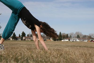 Side view of girl doing cartwheel on field against sky