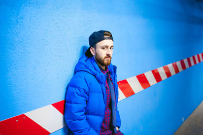 Portrait of young man standing against blue wall