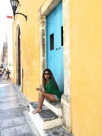 Full length portrait of woman sitting at entrance of building