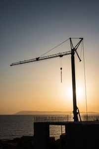Silhouette, outline of the crane on the construction site against the setting sun and the sea.