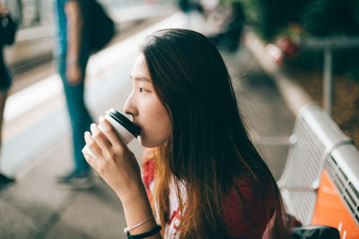 Side view of young woman drinking coffee at railroad station