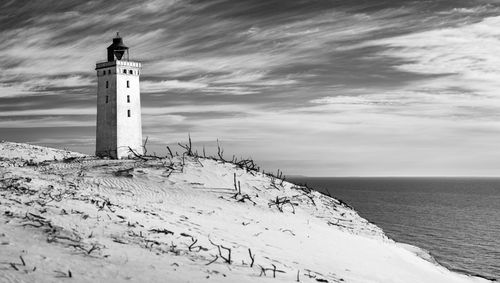 Lighthouse on beach by sea against sky