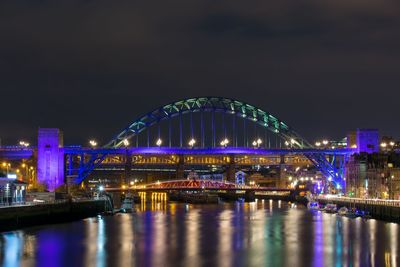 Illuminated bridge over river against sky at night