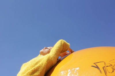 Woman leaning on yellow wall against clear blue sky