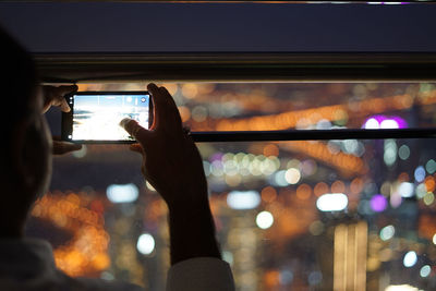 Man photographing illuminated smart phone at night