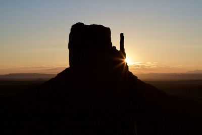 Silhouette person on rock against sky during sunset