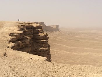 Woman on rock formation in desert against clear sky