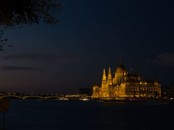 View of illuminated buildings by river against sky in city