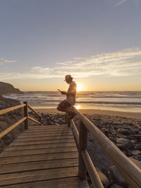 Portugal, senior man sitting on railing at the beach, reading